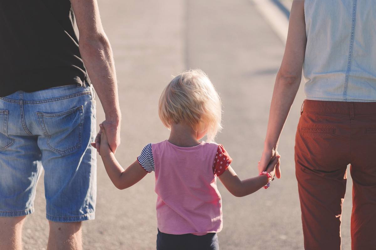 Mother, father and a young child, seen from behind, walking hand in hand down a sunlit path